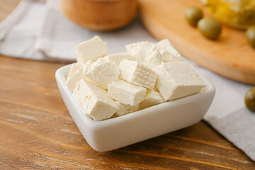 Bowl with tasty feta cheese on wooden background, closeup