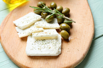 Board with tasty feta cheese, rosemary and olives on color wooden background