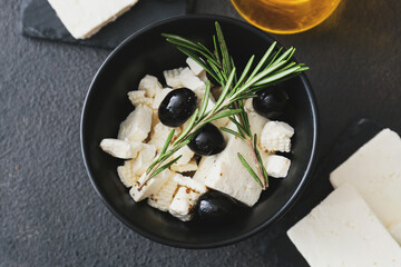 Bowl with tasty feta cheese, rosemary and olives on dark background
