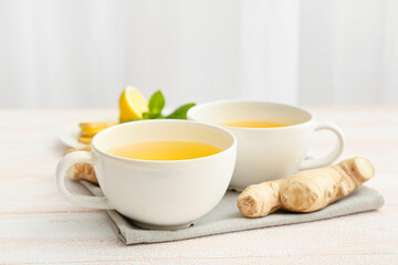 Cups of tea with ginger, mint and lemons on light wooden background