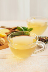 Cups of tea with ginger and mint on light wooden background