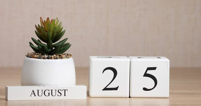 Wooden calendar with an important event for August 25, a woman's hand sets the date on the calendar. Summer season.
