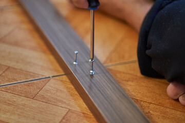 Detail of screwdriver with screw in wood. Assembling furniture at home. Carpentry