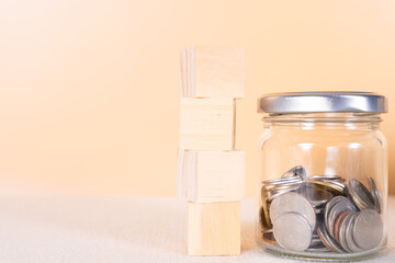 Wooden block stack and coin inside jar isolated orange background. Saving money and investment concept.