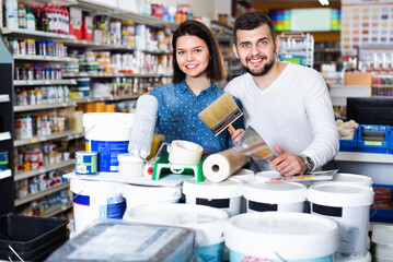 Smiling cheerful couple purchasing tools for house improvements in paint supplies store