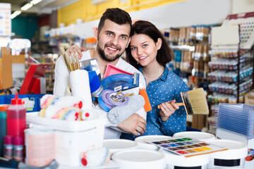 Cheerful couple purchasing tools for house improvements in paint supplies store