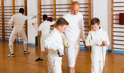 Trainer demonstrating to young athletes stances and movements with rapier during fencing workout