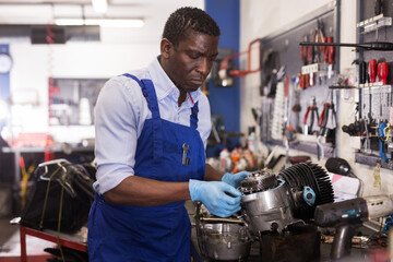 Afro american worker in overalls inspects a motorcycle engine. High quality photo