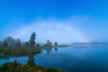 unusual natural phenomenon with a rainbow of fog over the lake, blurred misty landscape in the morning, blurred background