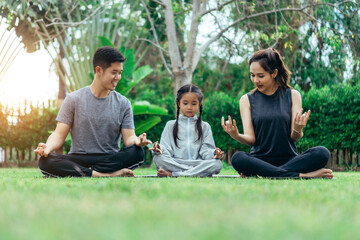 Happy Asian family is spending their holidays enjoying yoga in park together happily.