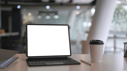 Close up view mock up computer tablet with blank screen and coffee cup on white office desk.