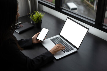 Cropped shot of businesswoman holding smart phone and searching information on laptop computer.