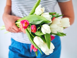 Woman holding beautiful bouquet with fresh colorful tulips on light background. Spring flowers. Florist, floristic. Copy space