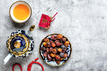 Popular food during Iftar - macadamia nuts, pistachios, walnuts, dry dates. Karan, rosary, teapot, bowl with black tea on concrete background Top view Flat lay Muslim holiday of holy month of Ramadan