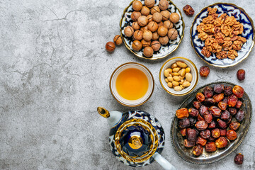 Popular food during Iftar - macadamia nuts, pistachios, walnuts, dry dates. Karan, rosary, teapot, bowl with black tea on concrete background Top view Flat lay Muslim holiday of holy month of Ramadan