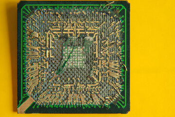An old broken computer CPU with a torn chip on a yellow background