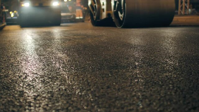 Strong plan of freshly laid asphalt. Two road rollers are laying asphalt. Steam from hot asphalt. Road repair in the city at night.