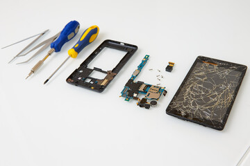 Disassembled smartphone and tools for its repair: tweezers and screwdrivers. The process describing...