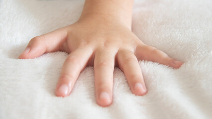 Closeup of left hand of a little girl placed on a white soft and cozy blanket