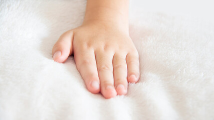 Closeup of left hand of a little girl placed on a white soft and cozy blanket