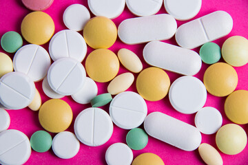 Lots of multicolored pills on a pink background copy space, close-up, top view