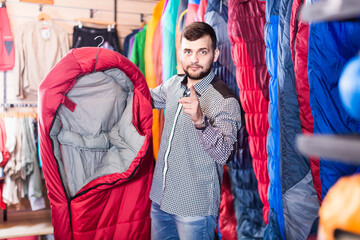 Smiling guy deciding on a new sleeping bag in sports equipment store