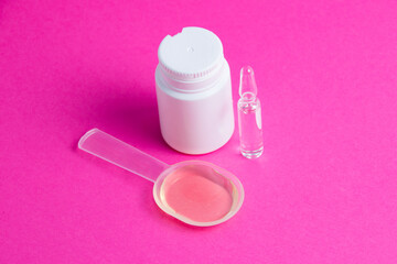 Ampoule with medicine, medicinal mixture and white jar of pills on pink background