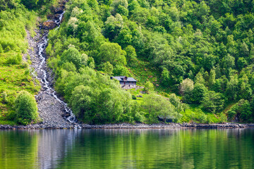 Fototapeta na wymiar Small cottage by a waterfall on the shore of a fjord