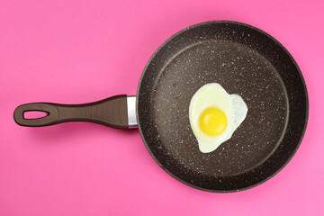 Fried egg in a frying pan on a pink background