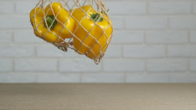 Mesh bag with peppers. A view of a mesh bag with organic yellow peppers on the table in the kitchen.