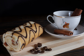 A mug of aromatic black coffee in a white cup with dessert, coffee beans and cinnamon sticks, on a wooden background. Coffee break. 