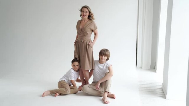 A mother and her two sons in beige and white clothes pose for a photo shoot 