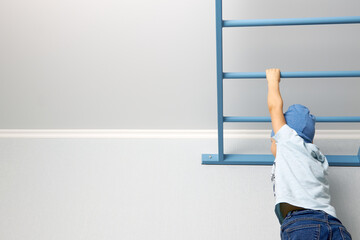 A child in a blue T-shirt and hat climbs a ladder near the ceiling. Home sports activities