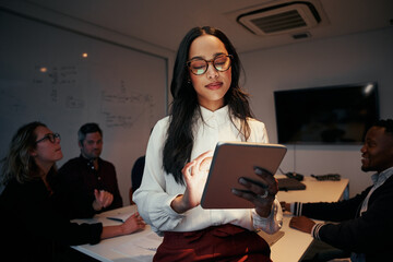 Portrait of a businesswoman using digital tablet with her team sitting at desk in meeting room - 429147494