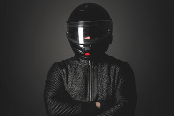 Serious motorbiker in a helmet with a crossed arms is standing on the dark background.
