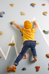 A child in jeans and a yellow T-shirt resolutely climbs up the climbing wall. Climbing wall in the...
