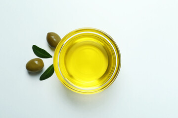 Bowl of oil, olives and leaves on white background