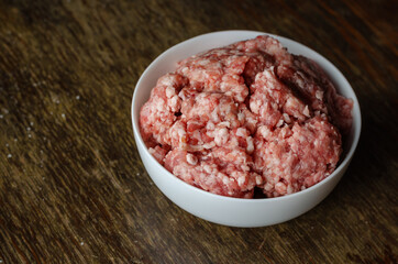 White ceramic bowl with raw minced meat on a dark wooden table.