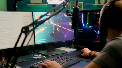 Pro gamer playing space shooter online video games using RGB keyboard and mouse during virtual championship. Streamer looking into monitors, talking with team on streaming chat