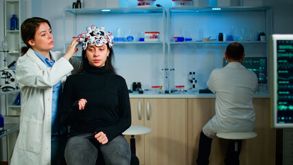 Medical lab technician adjusting eeg headset monitoring brain functions, descovering diagnosis of disease. Team of scientists researchers working late night in neurology clinic for woman health