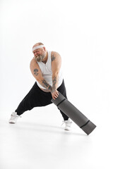 Obraz premium Happy fat man with big belly and tattos in sports wear with exercise mat