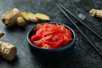 Bowl with red pickled ginger and chopsticks on black smokey background