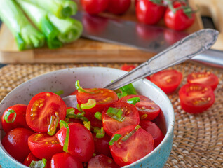 A bowl with fresh tomato salad topped with olive oil and spring onions