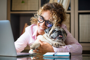 Woman work at home with laptop computer in smart working business modern job activity with her adorable best friend pug dog together with love and friendship - online free office lifestyle