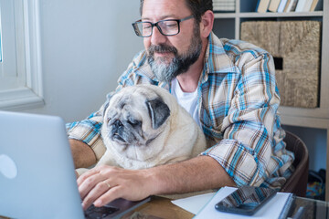 Portrait of mature man and dog working together at laptop computer with love and friendship - modern job lifestyle in home office - concept of online work and new job career for businessman