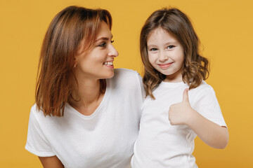 Happy woman in basic white t-shirt have fun with cute child baby girl 5-6 years old show thumb up Mommy little kid daughter isolated on yellow color background studio Mother's Day love family concept