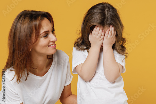 Happy woman in white t-shirt have fun with cute child baby girl 5-6 years old cover face. Mommy little kid daughter isolated on yellow orange color background studio. Mother's Day love family concept.