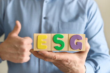 Businessman holds wooden cube blocks with the abbreviation ESG, the concept of checking the company...