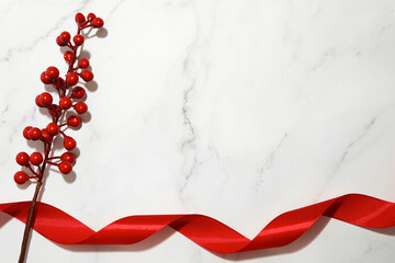 Red berries with red ribbon on white stone background. Simple minimalist holiday themed composition. Side borders from top view. Empty space for text. Copy space.