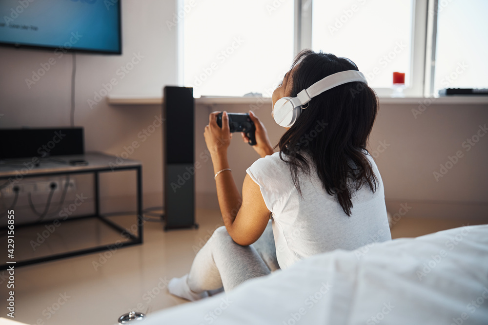 Wall mural young woman in headphones playing video game at home